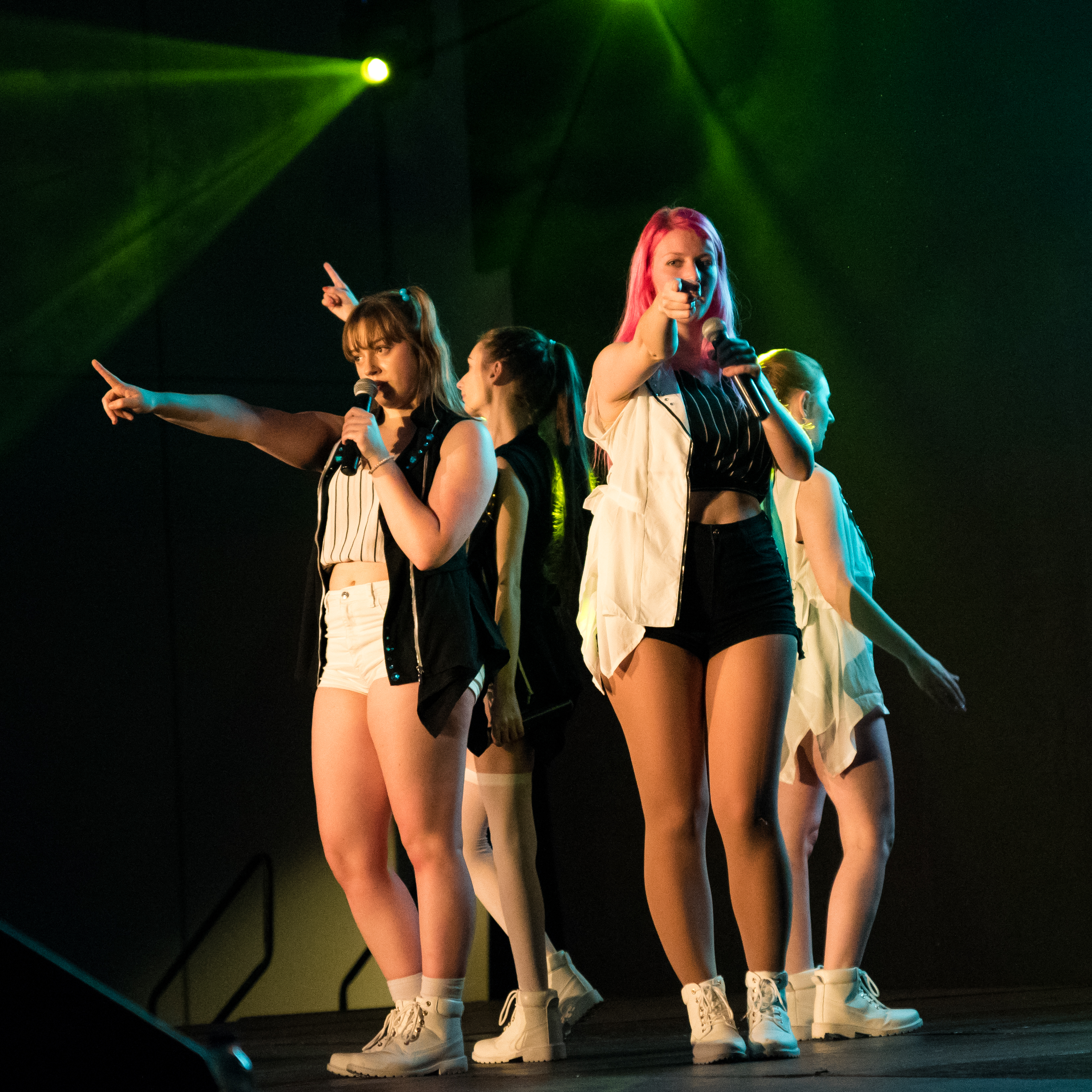 girl dancers on stage with a microphone poiting at the crowd